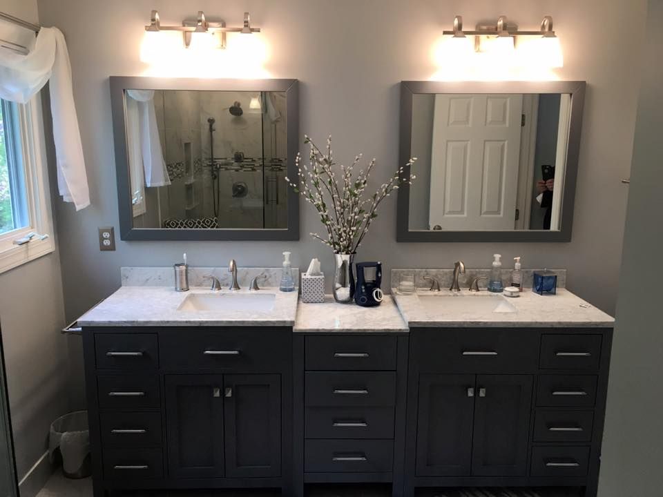 Gray bathroom with two vanities, mirrors, and lights. Shower visible behind the left mirror, decor and supplies on the count