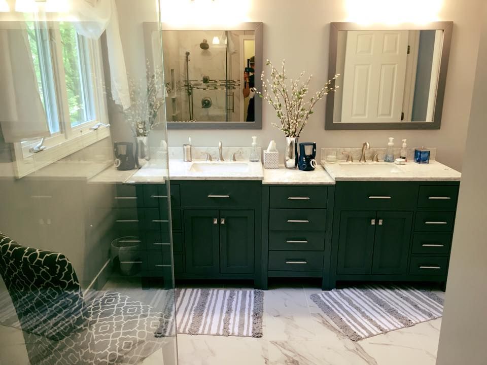 Two dark green bathroom vanities with marble countertops, matching mirrors, and rugs.