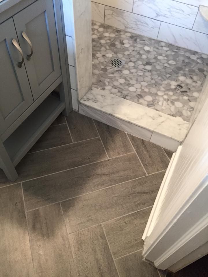 Bathroom with gray tile floor in a herringbone pattern; marble shower with pebble tile floor and gray vanity.