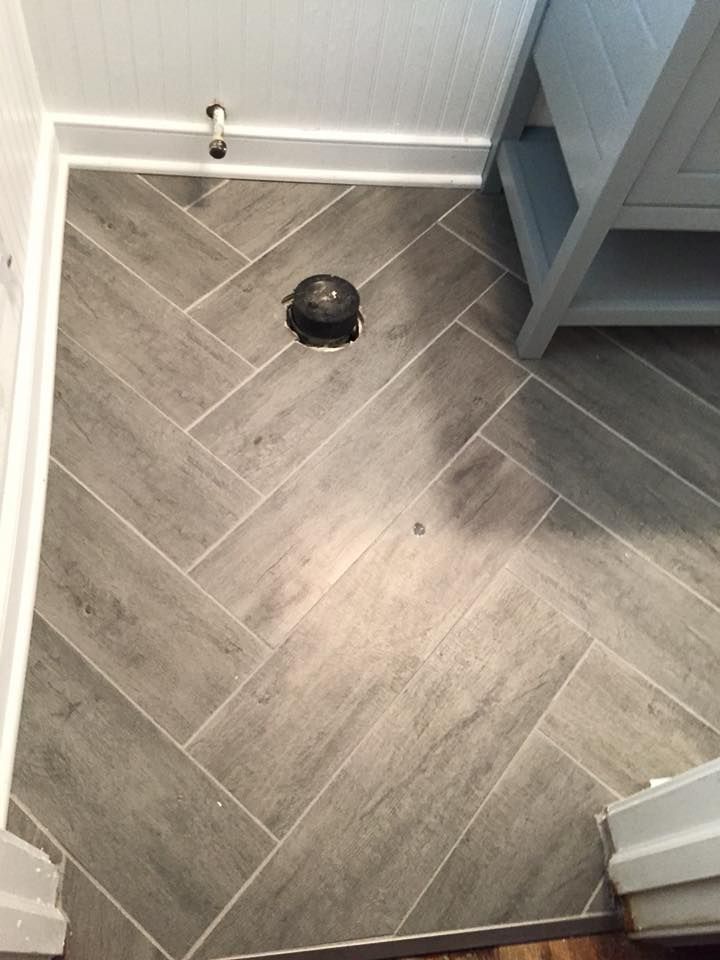 Gray herringbone tile floor in a bathroom corner, next to a vanity.