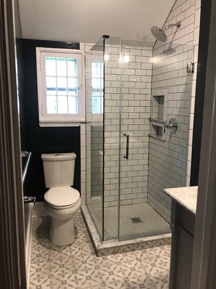 Modern bathroom with a glass shower, toilet, patterned floor, and white subway tile.