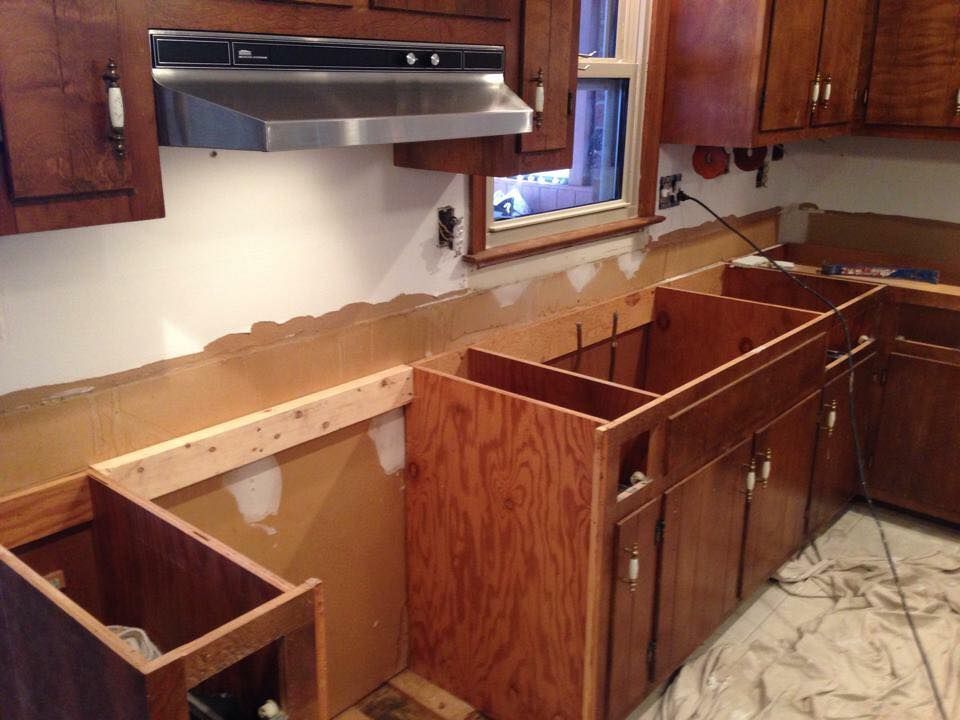 Kitchen cabinets in various stages of assembly; unfinished. Brown wood with exposed walls.