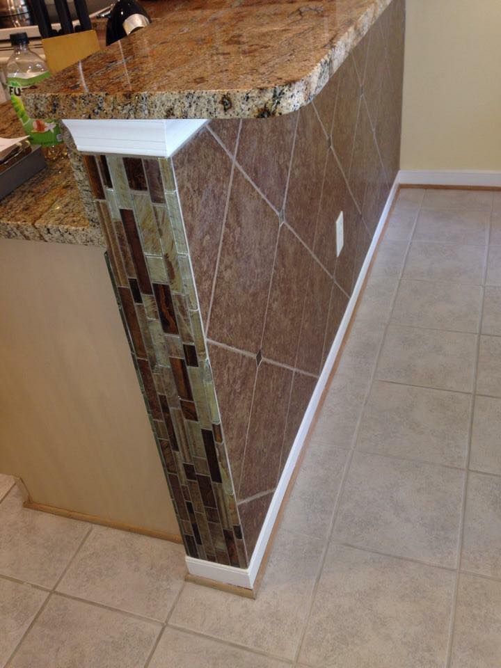 Kitchen island with brown tile and granite countertop, accented with glass mosaic and white trim.