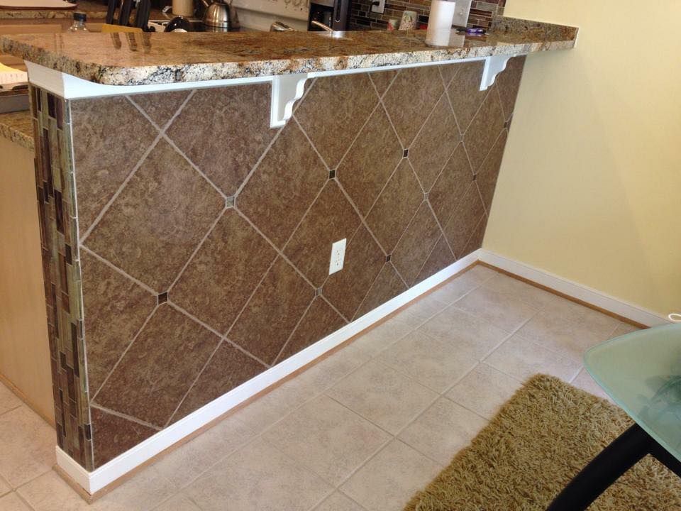 Kitchen island with brown tiled face, white trim, and granite countertop.