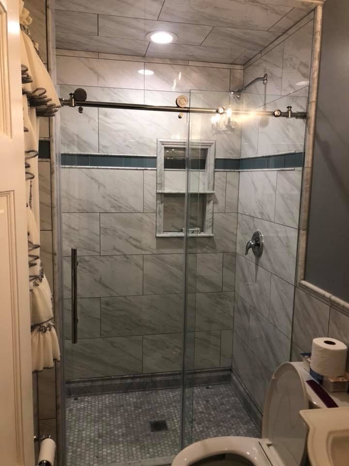 A bathroom with a tiled shower, glass door, toilet, and white and blue accents.