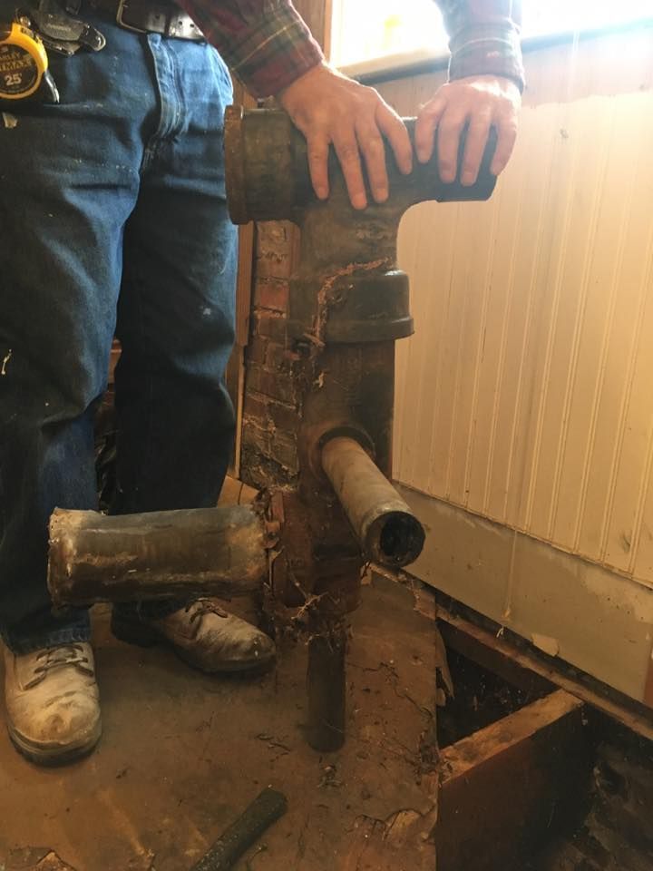 Man holding a large, rusty pipe system near a wooden wall and floor during renovation.