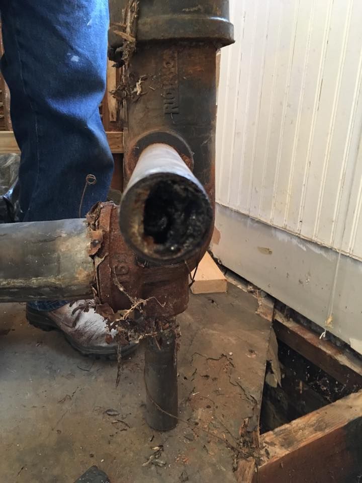 Corroded plumbing pipe with blocked opening, likely waste disposal. Person in blue jeans visible.