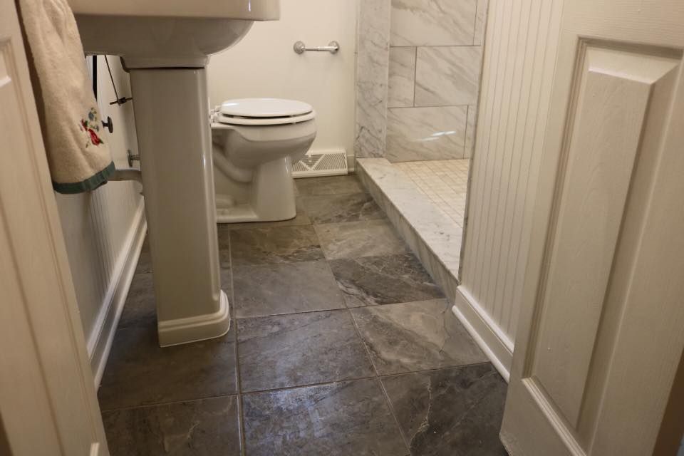 Bathroom with toilet, sink, and tiled shower. Stone tile floor, white trim, and door.