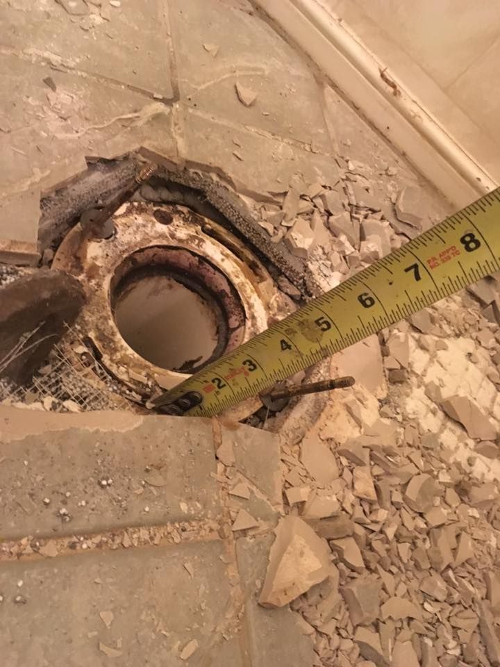 Toilet flange surrounded by broken tile, measuring tape at 3 inches.