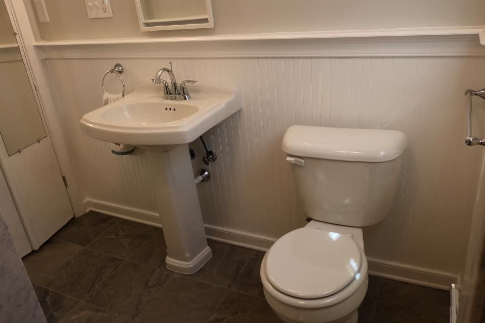 Bathroom with white pedestal sink, toilet, and wainscoting on dark tile floor.