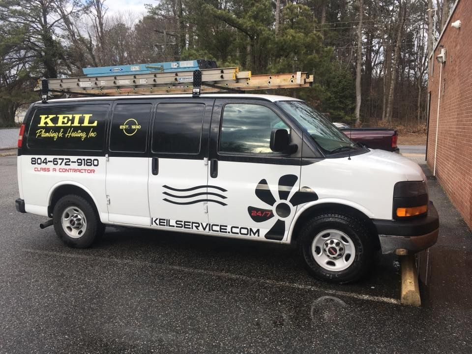 White Keil Heating & Cooling van with ladder, parked near a brick building.