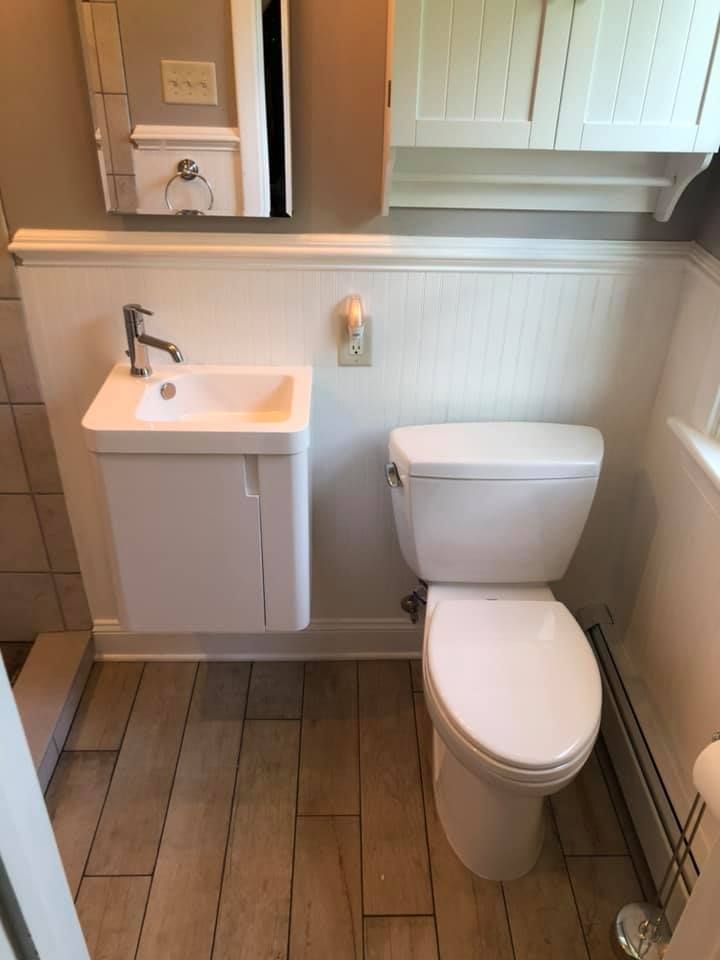 Small white bathroom with wall-mounted sink, toilet, and wooden floor.