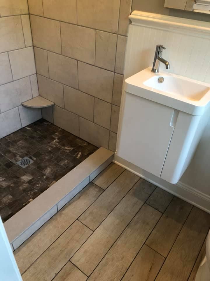 Bathroom with a shower stall and small sink. Light wood-look flooring. Beige tile walls.