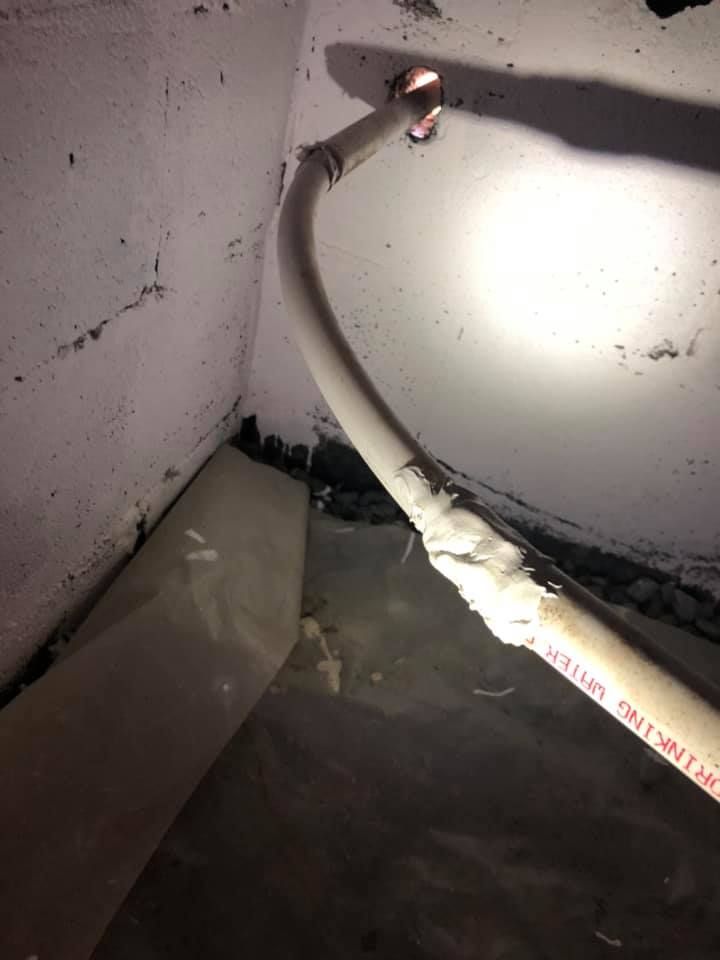 White plastic pipe in a basement corner, insulation spray on the pipe, dark walls.
