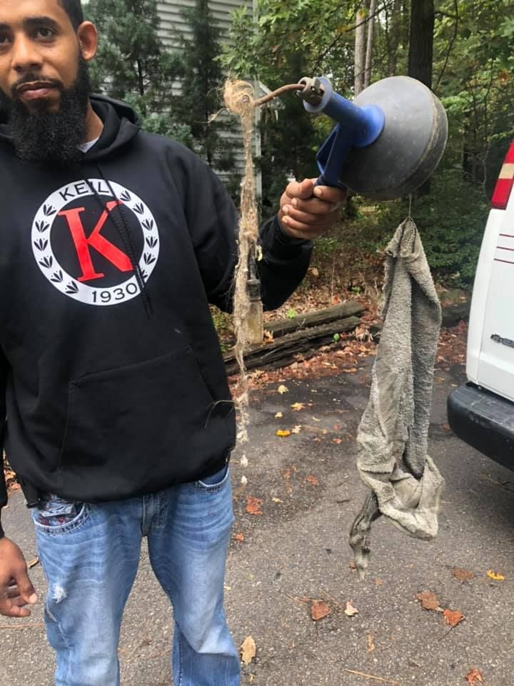 Man holding drain cleaner with debris, outside near a vehicle and trees.