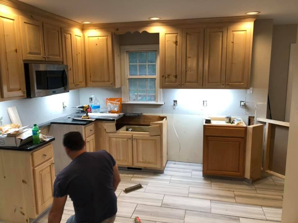 Man installs kitchen cabinets in room with wood cabinets, new flooring.