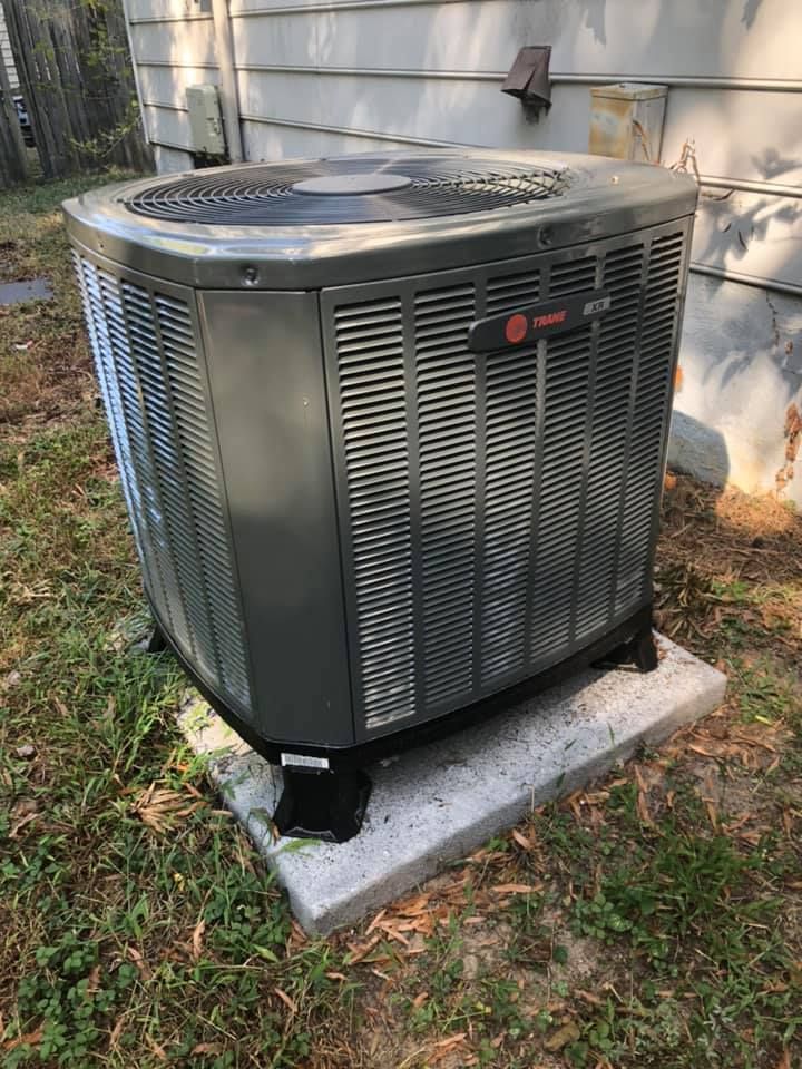 Gray Trane air conditioning unit on a concrete slab in a grassy yard.