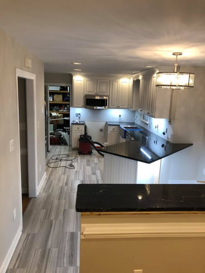 A partially renovated kitchen with new countertops, cabinets, and flooring; a hallway leads to a pantry.