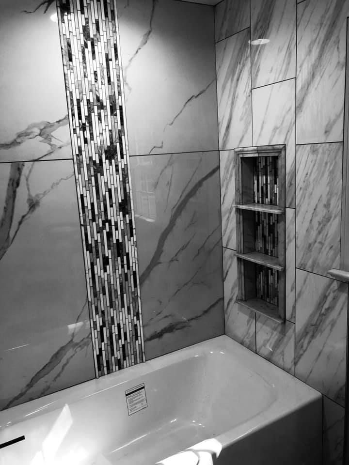Bathroom with white bathtub, marble-look tiled walls, and decorative mosaic tile strip. Includes a recessed shelf unit.