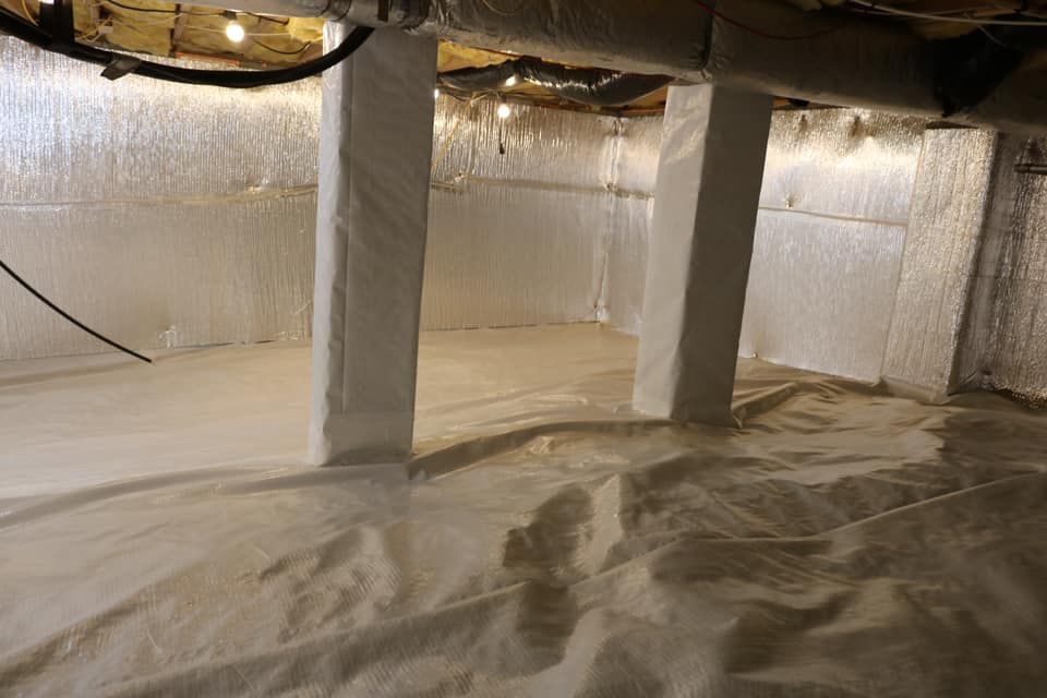 Crawl space insulated with white material, three white support columns, silver reflective walls, dim lighting.