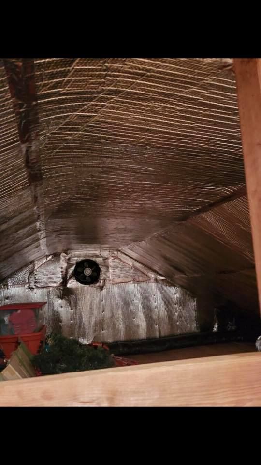 Attic interior with metal walls and ceiling covered in reflective insulation; fan visible.