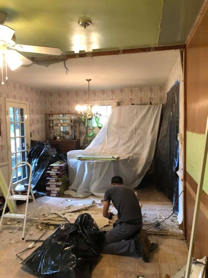 Person working on a room renovation; partially demolished wall, covered furniture, debris on floor.