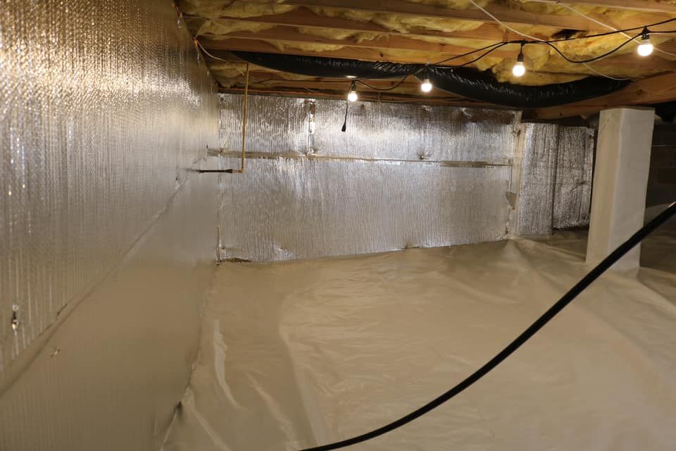 A crawl space with foil-backed insulation on the walls, a white vapor barrier on the floor, and string lights.