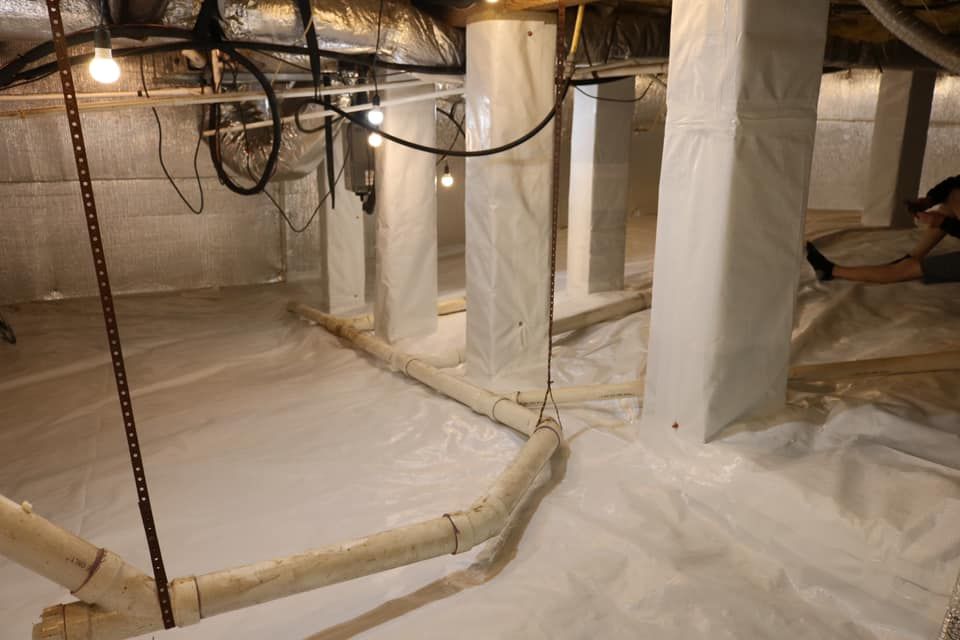 White crawlspace with plastic vapor barrier, wrapped support columns, and pipes.