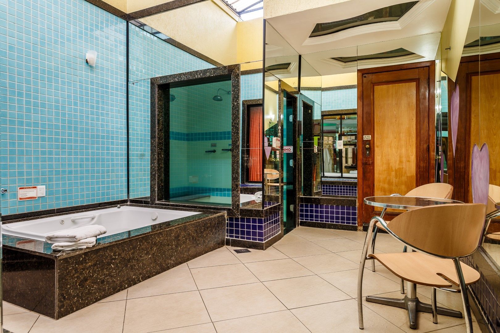 Um quarto de motel com jacuzzi, azulejos azuis, espelhos e claraboia.