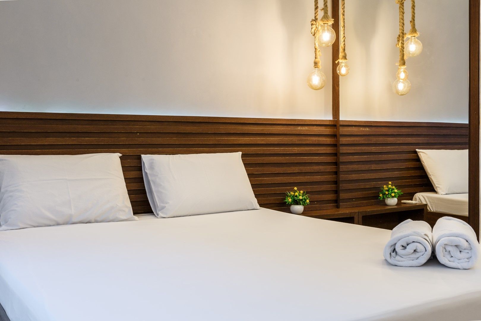 Um quarto de hotel com cama branca, cabeceira de madeira e luminárias pendentes.