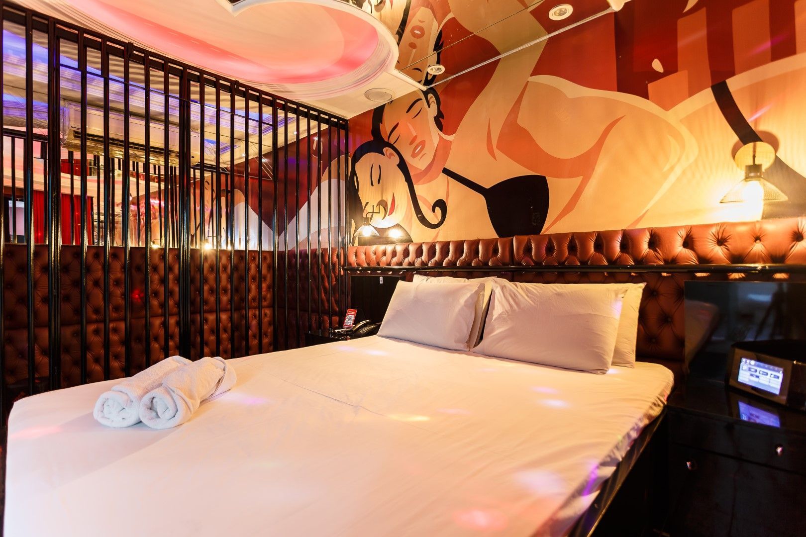 Quarto de hotel com cama, arte erótica na parede, teto tipo gaiola e toalhas.