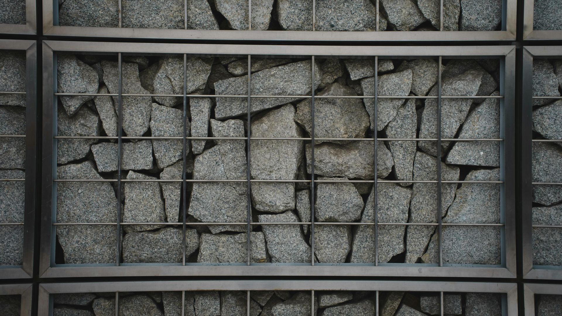 Gray stone wall with a grid of dark metal bars over broken, uneven stone panels