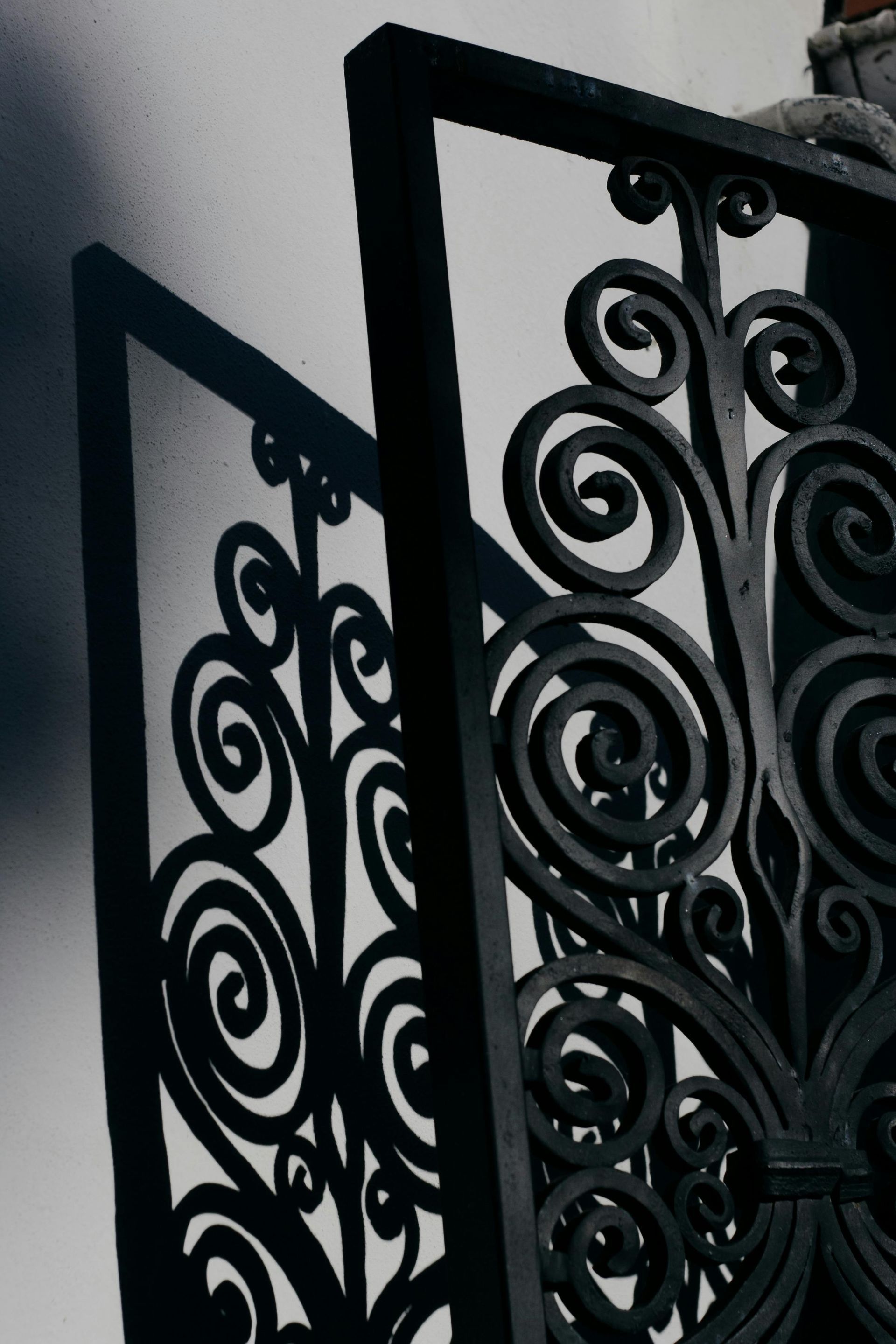 Black wrought-iron spiral gate or railing on a light gray wall