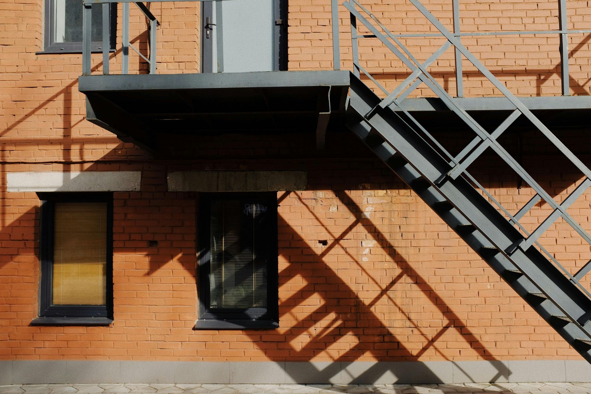 Brick building facade with black metal stairs and balconies casting diagonal shadows