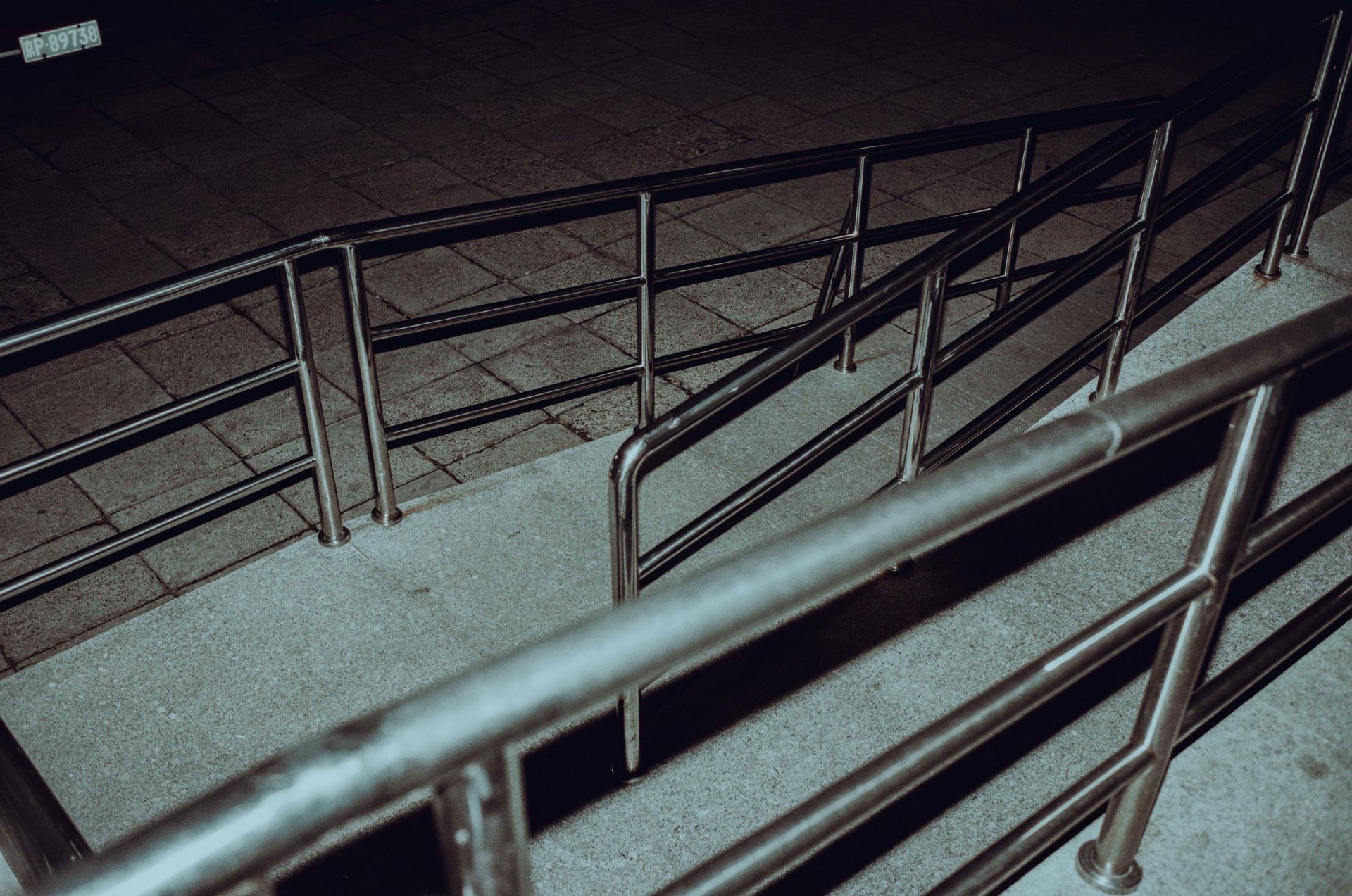 Metal railings along a sloped concrete ramp at night, viewed from above.