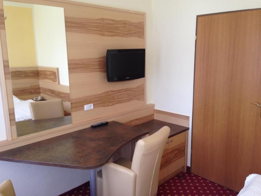 Hotelzimmer mit Schreibtisch, Spiegel, Fernseher und geschlossener Tür.