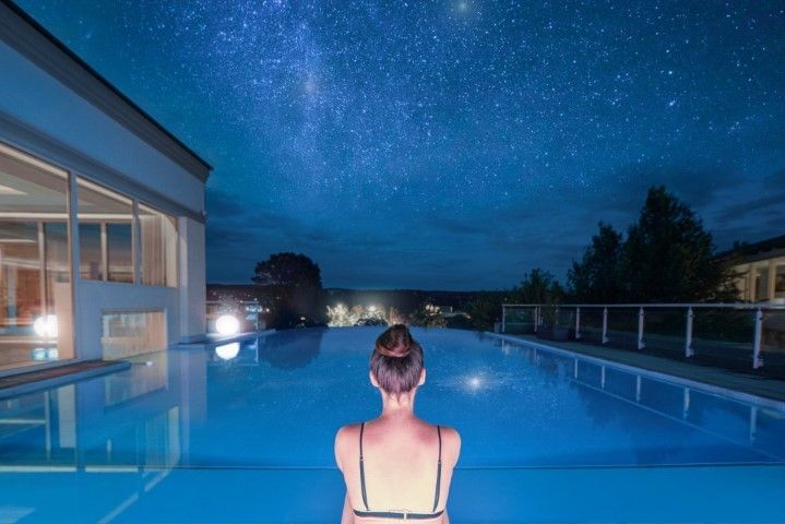 Frau blickt von einem Außenpool in einem Spa aus in den Sternenhimmel.