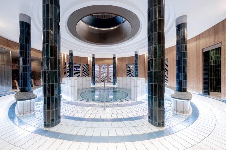 Ein luxuriöses Spa mit rundem Pool, blau gefliesten Säulen und einem Oberlicht.