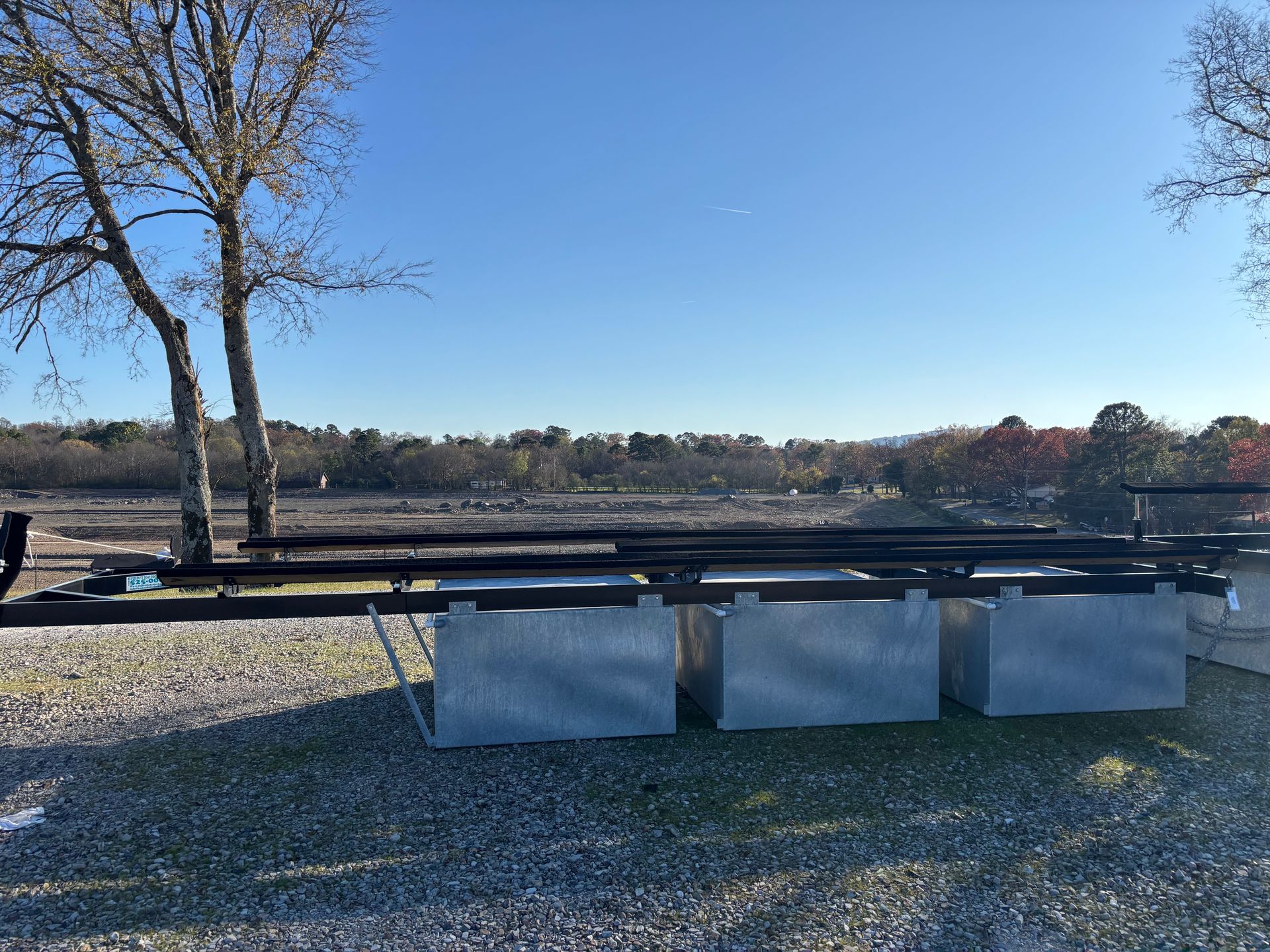 A boat trailer is parked in a gravel lot next to a tree.