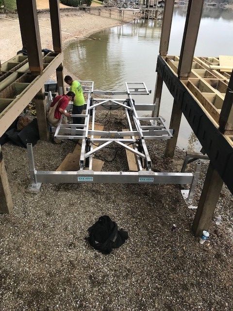 Two men are working on a boat lift near a body of water