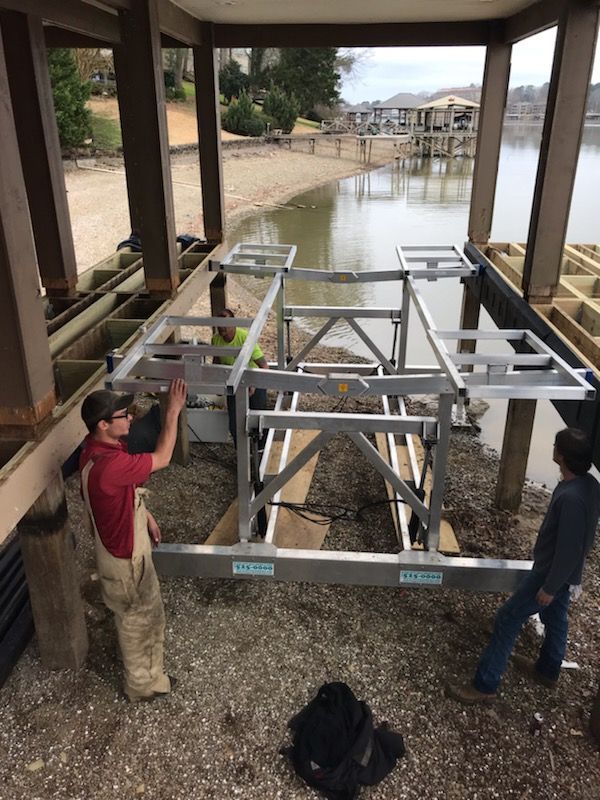 A group of men are working on a boat lift under a dock.