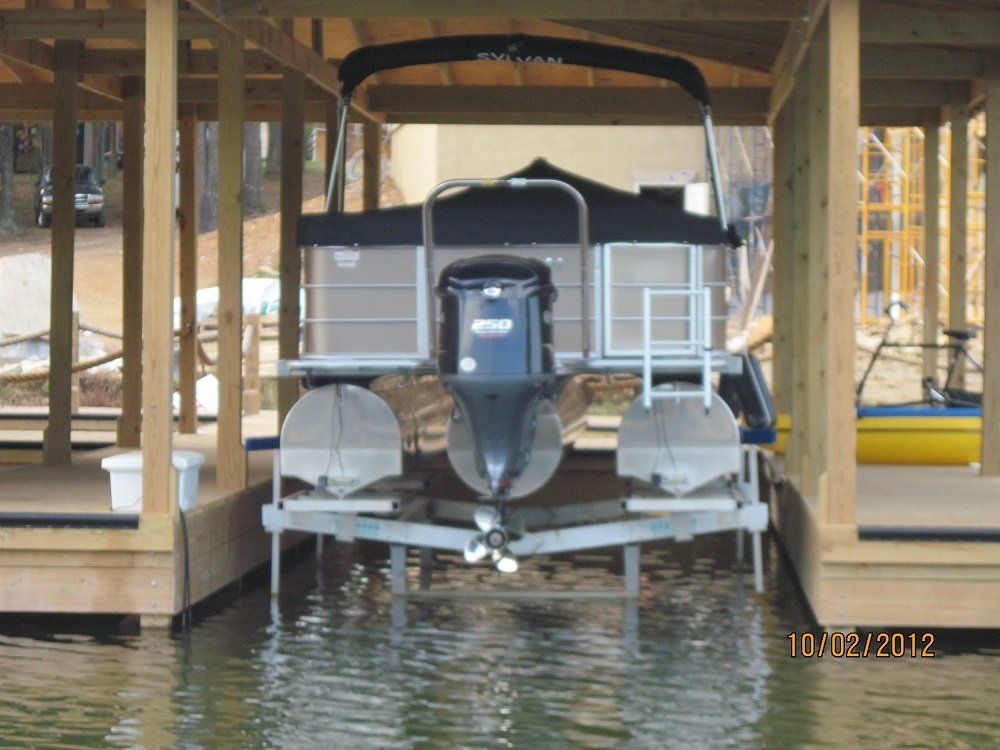 A pontoon boat is docked under a wooden structure in the water