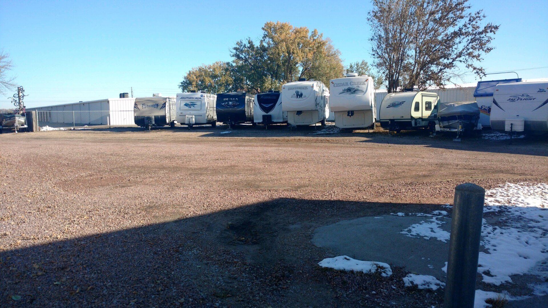 A row of rvs are parked in a gravel lot