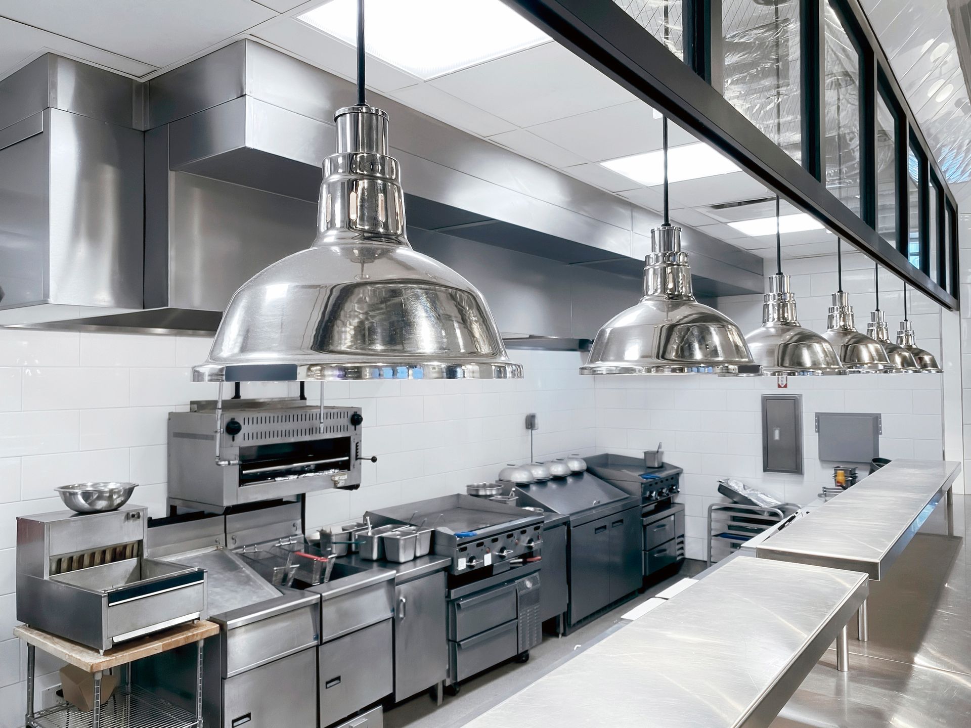 A kitchen with a lot of stainless steel appliances and lamps hanging from the ceiling.