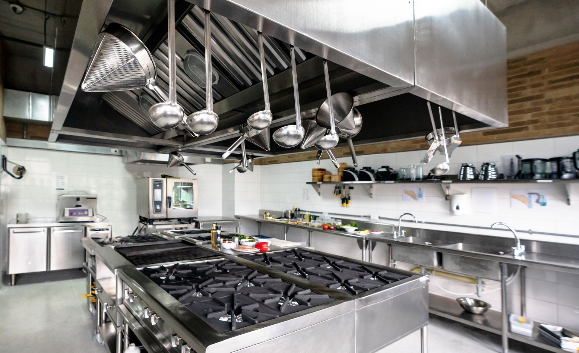 A kitchen with a lot of stainless steel appliances and utensils hanging from the ceiling.