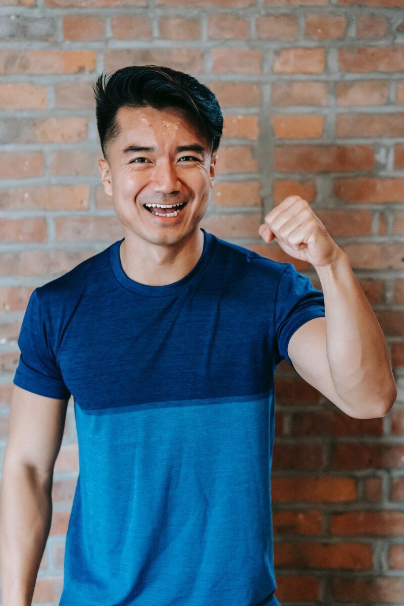 A man in a blue shirt is flexing his muscles in front of a brick wall.