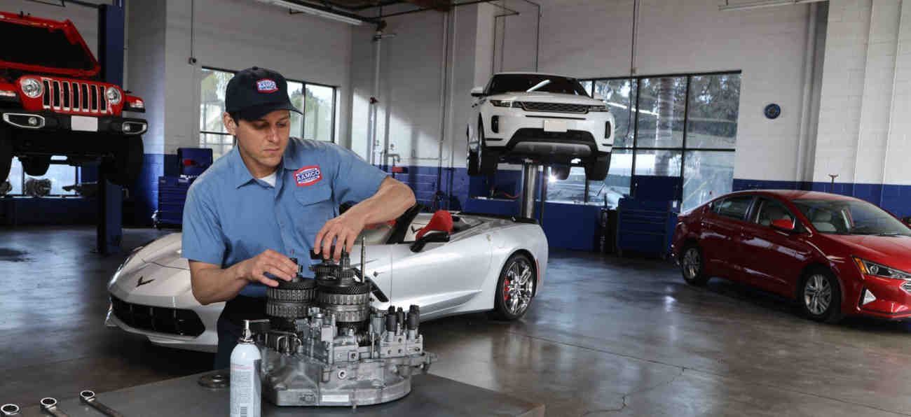 Mechanic in blue shirt working on engine in garage with sports cars on lifts and floor