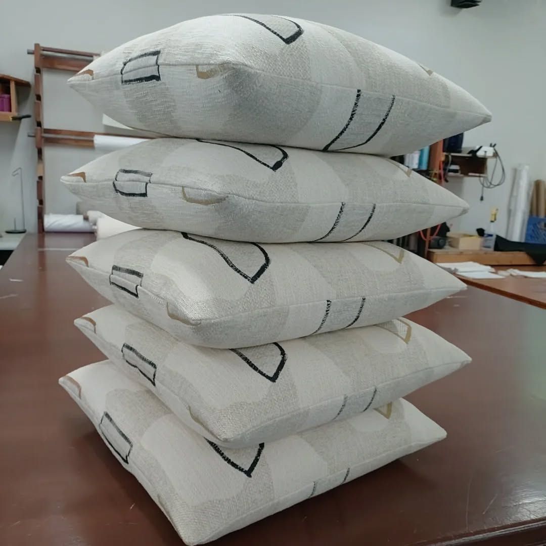 Four white fabric sandbags stacked on a wooden table in a workshop.