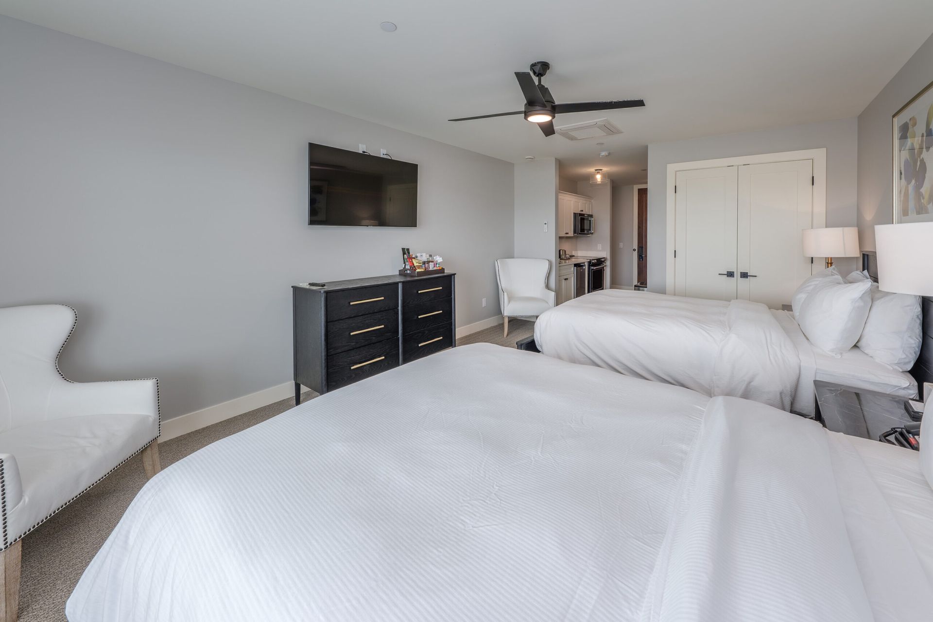 A hotel room with two beds , a chair , a dresser and a flat screen tv.