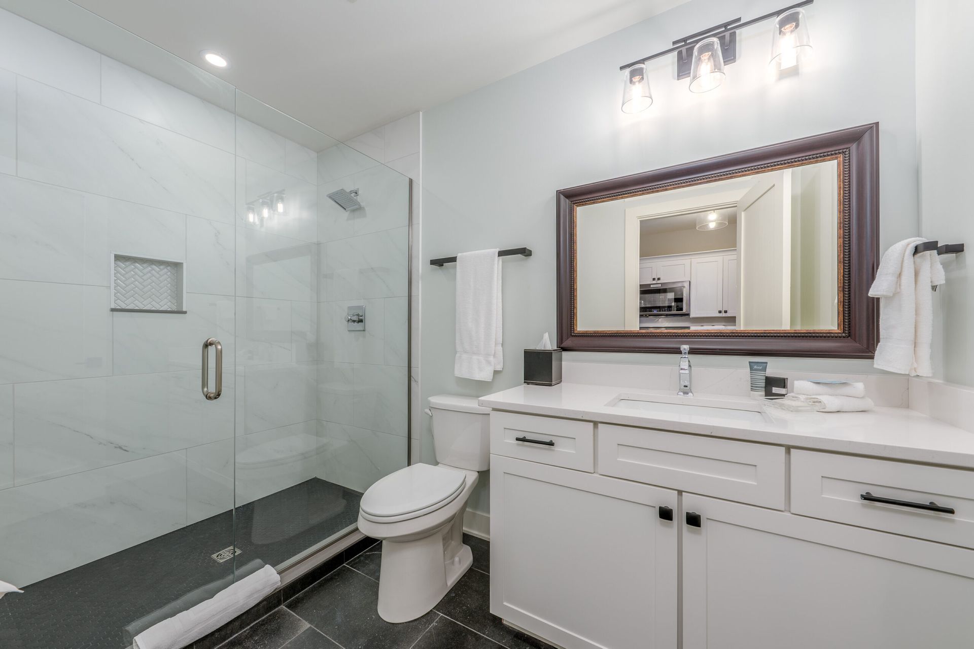 A bathroom with a toilet , sink , mirror and walk in shower.